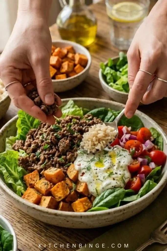 A beautiful, vibrant burger bowl in a ceramic dish featuring lean ground beef, sliced avocado, cherry tomatoes, red onions, and a drizzle of secret sauce over a bed of fresh greens.
